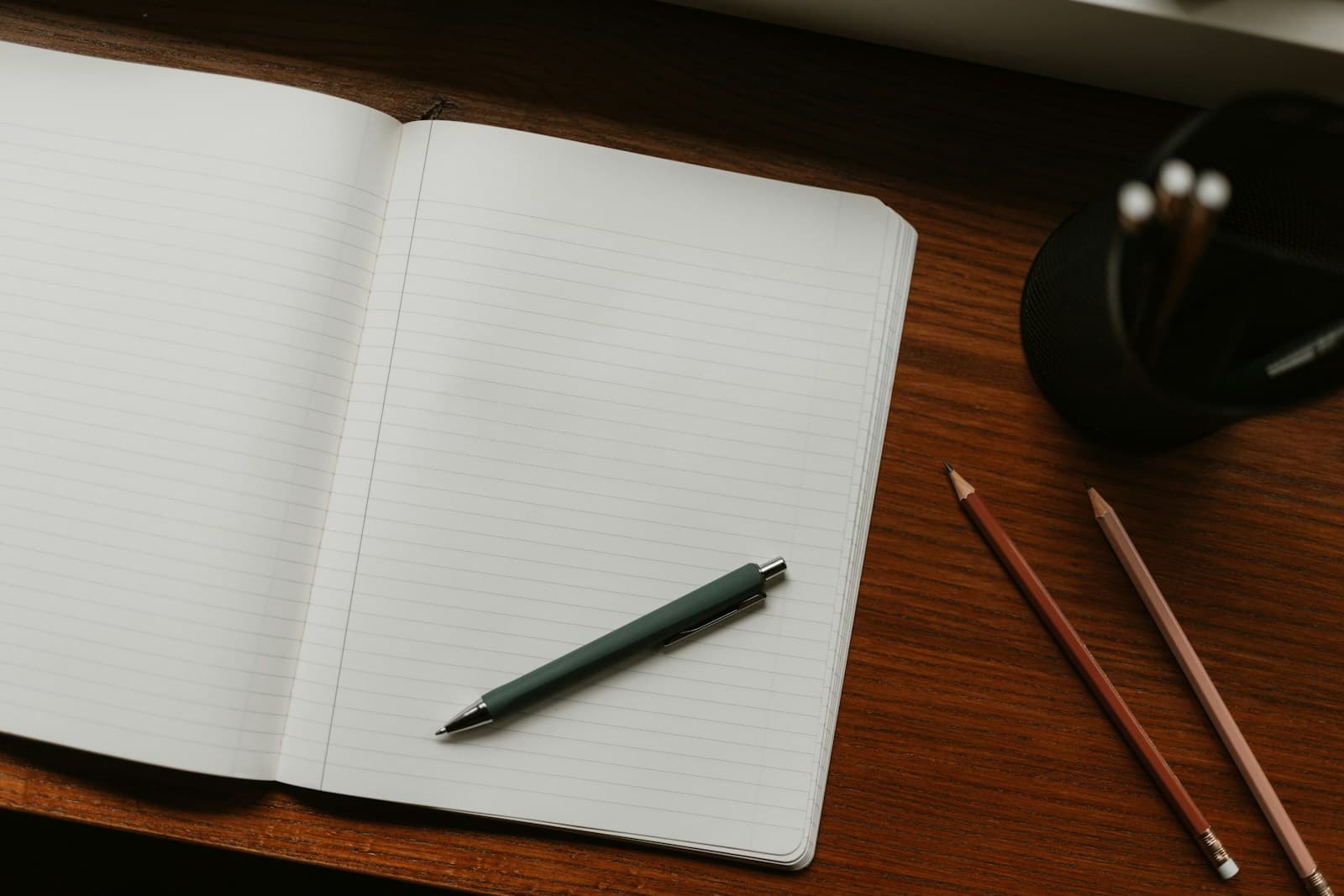 Open lined notebook with a pen and pencils on a wooden desk